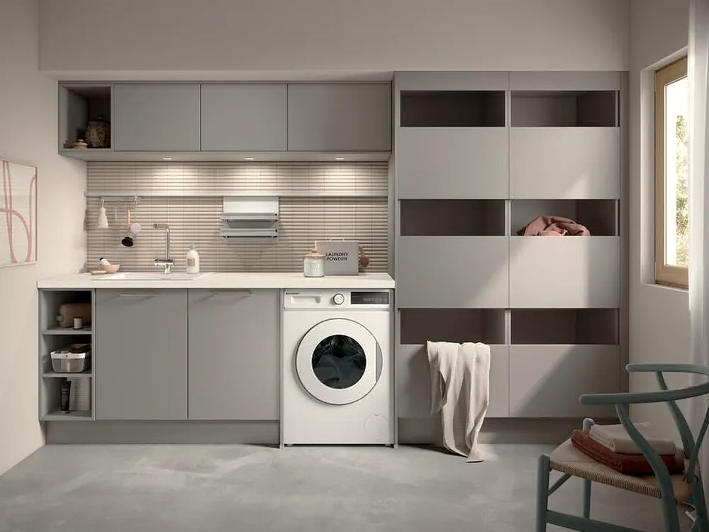 Hauswirtschaftsraum von Häcker in Grau mit Waschmaschine, durchgehender Arbeitsfläche, Hochschränken und offenen Fächern für Wäschekörbe